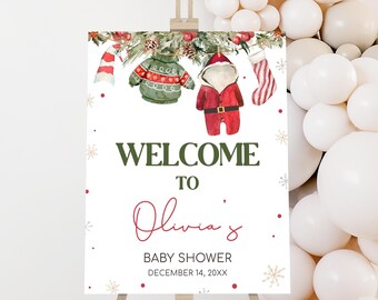 May include: A welcome sign for a baby shower, featuring watercolor illustrations of Christmas sweaters, Santa Claus, and a stocking. The sign reads "Welcome to Olivia's Baby Shower" with the date December 14, 20XX.