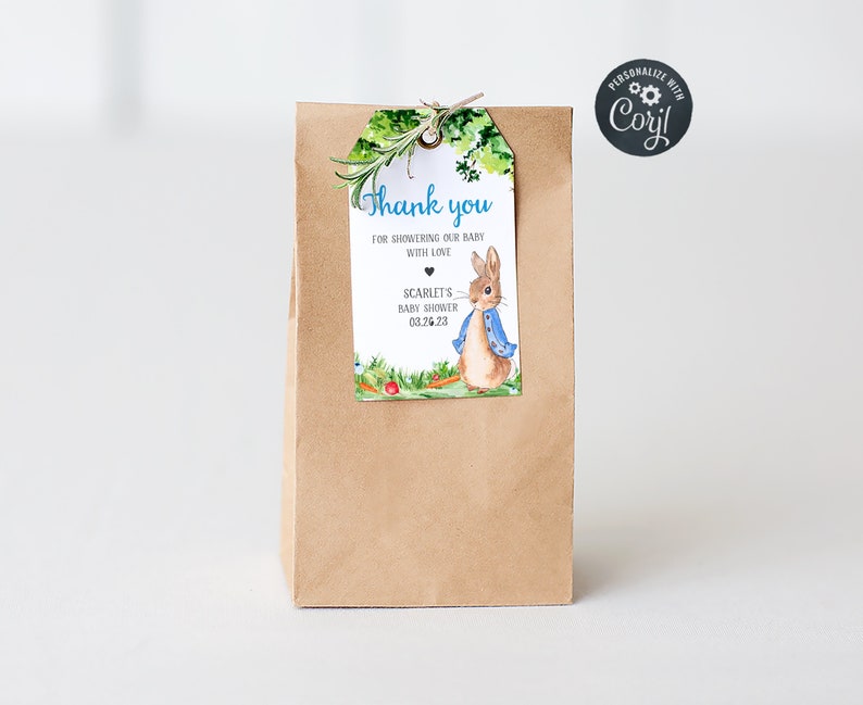 Puede incluir: Una bolsa de regalo de papel marr&oacute;n con una etiqueta de agradecimiento adjunta. La etiqueta presenta una ilustraci&oacute;n de acuarela de un conejo con una chaqueta azul y el texto "Gracias por consentir a nuestro beb&eacute; con amor, Baby Shower de Scarlet 03.26.23".