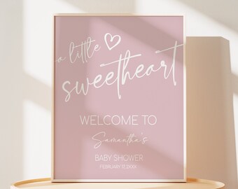 Könnte beinhalten: Ein rosa Babyparty-Schild mit weißem Text, der "a little sweetheart" mit einem Herzsymbol lautet. Das Schild sagt auch "Willkommen zur Babyparty von Samantha" und das Datum "Februar 17, 20XX".