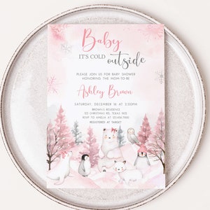 Op de afbeelding: Een uitnodiging voor een babyshower met een winterthema. De uitnodiging bevat de tekst "Baby It's Cold Outside" in roze script. De uitnodiging bevat illustraties van ijsberen, pingu&iuml;ns en een uil. De uitnodiging ligt op een wit bord.