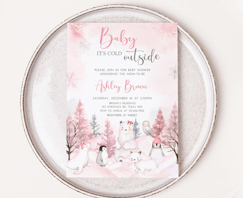 Op de afbeelding: Een uitnodiging voor een babyshower met een winterthema. De uitnodiging bevat de tekst "Baby It's Cold Outside" in roze script. De uitnodiging bevat illustraties van ijsberen, pingu&iuml;ns en een uil. De uitnodiging ligt op een wit bord.