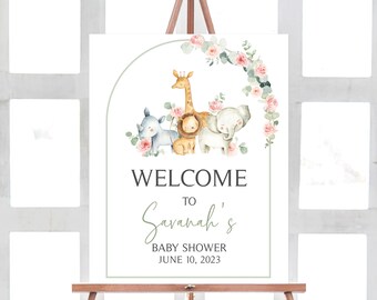 May include: Welcome to Savannah's Baby Shower sign with a green and pink floral wreath and a watercolor illustration of a giraffe, lion, and elephant. The sign says "Welcome to Savannah's Baby Shower June 10, 2023".