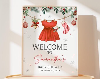 May include: A framed baby shower sign with a red dress, stocking, and ornaments hanging from a string. The sign reads "WELCOME TO Samantha's BABY SHOWER DECEMBER 13, 2XXX" in a festive font, with snowflake accents.
