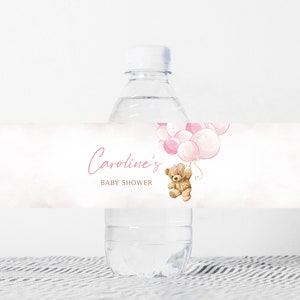 May include: Water bottle label with a pink and white watercolor background. The label features a teddy bear holding pink balloons and the text "Caroline's Baby Shower".
