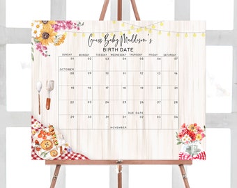 Op de afbeelding: Een wit houten bord met een gedrukte kalender erop. De kalender is voor oktober en november. Het bord heeft een bloemmotief met zonnebloemen en een glazen pot met bloemen. De tekst op het bord zegt "Raad de geboortedatum van baby Maddison".