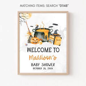 The image is a framed poster with a Halloween-themed illustration, including a pot, broom, jack-o-lantern, and bats. The poster welcomes visitors to Maddison's baby shower and provides the date and time as October 26, 2XX.