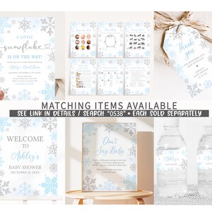 Puede incluir: Decoraciones para baby shower con dise&ntilde;o de copos de nieve en azul claro, plateado y blanco. El conjunto incluye invitaciones, juegos, un letrero de bienvenida, etiquetas de regalo y etiquetas para botellas de agua. El texto incluye "A Little Snowflake is on the Way!" y "Ashley's Baby Shower".