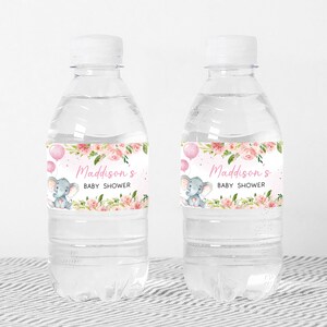 Pu&ograve; includere: Due bottiglie d'acqua in plastica trasparente con etichette floreali rosa e verdi. Le etichette mostrano un piccolo elefante grigio che tiene palloncini rosa e il testo "Baby Shower di Maddison".
