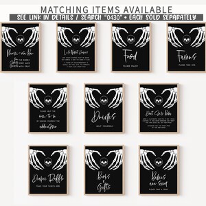 K&ouml;nnte beinhalten: Eine Sammlung gerahmter schwarz-wei&szlig;er Schilder mit Halloween-Motiven. Jedes Schild zeigt ein Skeletthand-Design mit einem Totenkopf und Text wie "Food", "Favors" und "Drinks". Die Schilder sind vor einem wei&szlig;en Hintergrund ausgestellt.