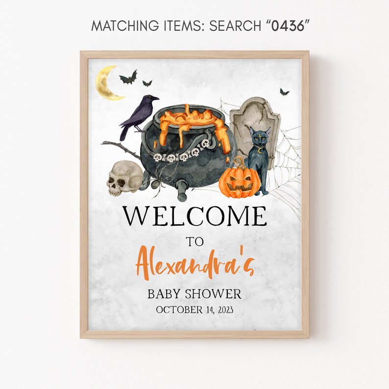 May include: A framed Halloween-themed baby shower sign. The watercolor design features a cauldron, black cat, pumpkin, skull, and the text "Welcome to Alexandra's Baby Shower October 14, 2023". The sign is in a light wood frame.