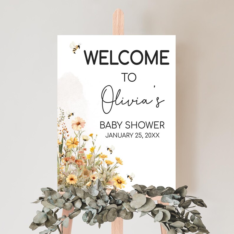 a baby shower sign with flowers and greenery