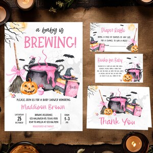A Halloween-themed baby shower invitation featuring a black cauldron, pumpkins, bats, and a broom, with a spooky and whimsical design.
