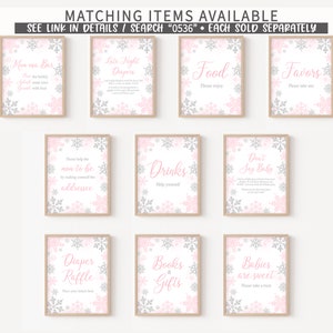K&ouml;nnte beinhalten: Eine Sammlung von gerahmten Schildern mit rosa und silbernen Schneeflocken-Designs. Die Schilder tragen Texte wie "Mom osa Bar", "Food", "Favors", "Drinks" und "Babies are sweet". Die Schilder sind f&uuml;r eine Babyparty.