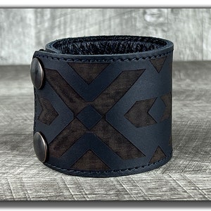 May include: Black leather cuff bracelet with a geometric pattern and two silver-toned snap closures.