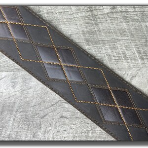 Peut inclure: Une sangle de guitare en cuir marron avec un motif en losange et des coutures jaunes.
