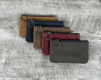 May include: Five leather zipper pouches in different colors, including brown, black, red, and gray. Each pouch has a small metal ring attached to the zipper.
