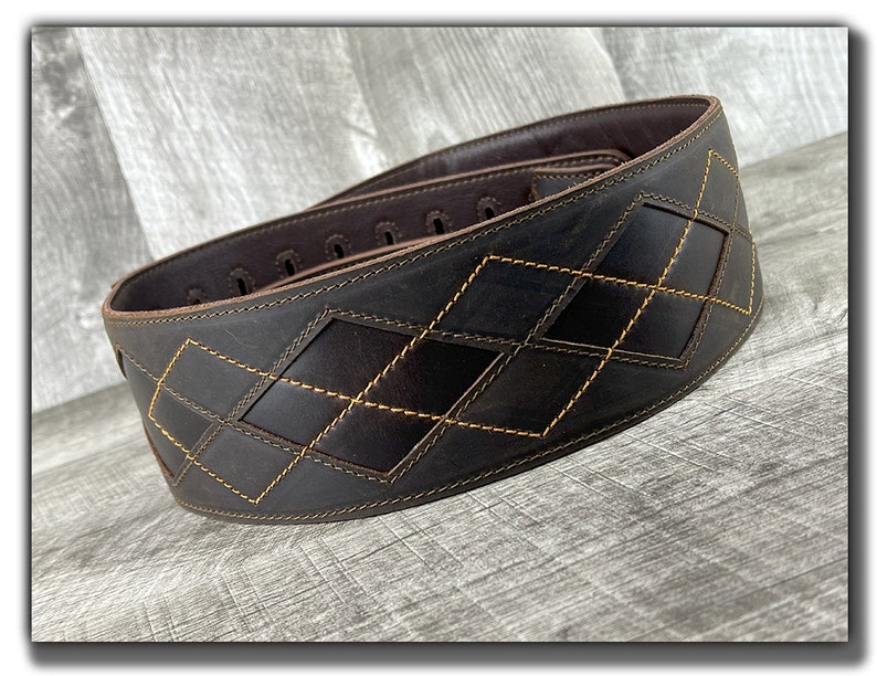 Peut inclure: Une sangle de guitare en cuir marron avec un motif en losanges cousu avec du fil jaune.