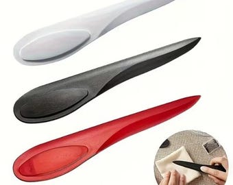 May include: A set of three plastic point turners in white, black, and red. Each tool features a smooth, elongated, tapered shape with a rounded handle section and a pointed tip, designed for pressing out corners in fabric projects and sewing.