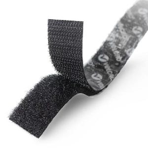May include: A black hook and loop fastener strip with a textured surface. The strip is partially separated, revealing the adhesive backing which features the white Velcro brand logo printed repeatedly along the length of the adhesive side.