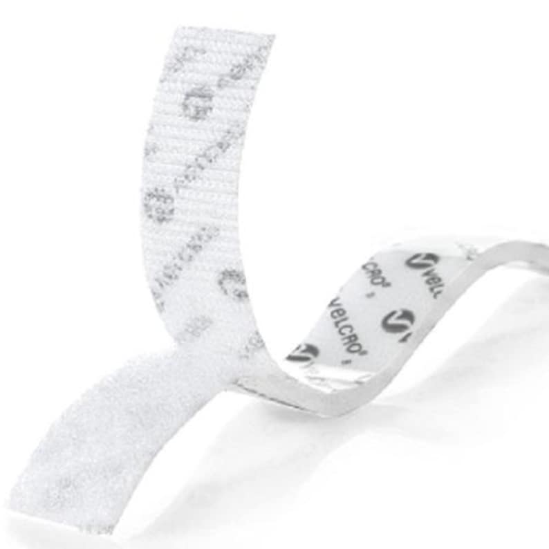 May include: A white adhesive hook and loop fastener strip with a textured surface. The backing paper is white and features the repeating black text and logo for VELCRO. The strip is partially peeled back to reveal the adhesive side and the fastener.