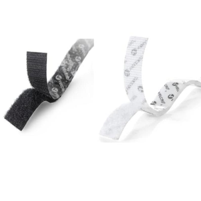 May include: Two strips of hook and loop fastener tape, one black and one white. Each strip features a textured surface on one side and a backing printed with the word Velcro and a circular logo. The strips are partially peeled apart to show the texture.