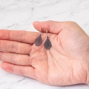May include: A pair of silver dangle earrings with a teardrop shape and a black, intricate, geometric design.