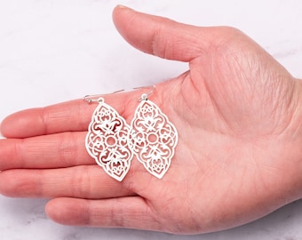 Peut inclure: Une paire de boucles d'oreilles en filigrane argentées avec un design délicat et complexe. Les boucles d'oreilles sont en forme de diamant et ont une goutte pendante.