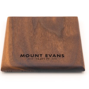 May include: A dark brown wooden coaster with the text "MOUNT EVANS - 14,271 FT -" engraved on the surface.