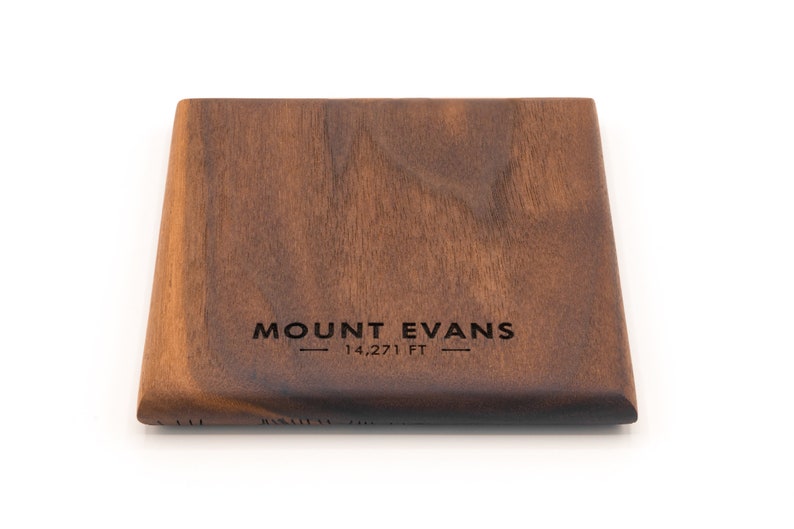 May include: A dark brown wooden coaster with the text "MOUNT EVANS - 14,271 FT -" engraved on the surface.