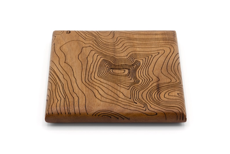May include: A square wooden coaster with a brown wood grain finish and a laser-etched design of topographic lines.