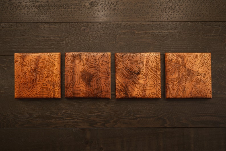 May include: Four wooden coasters with a natural wood grain finish and a unique topographic map design.