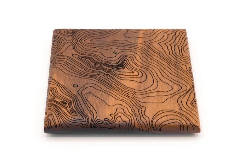May include: A square wooden serving board with a dark brown wood grain and a black topographic map design.