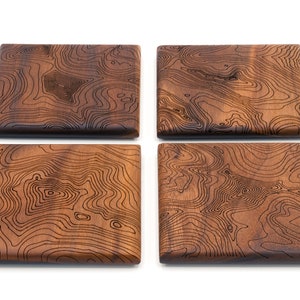 May include: Set of four square wooden coasters with a dark brown wood finish and a laser-etched topographic map design.