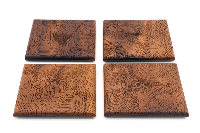 May include: Set of four square wooden coasters with a dark brown wood finish and a laser-etched topographic map design.