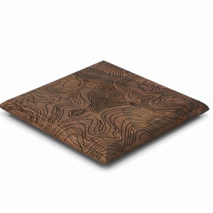 May include: A square wooden coaster with a brown wood grain finish and a black topographic map design.