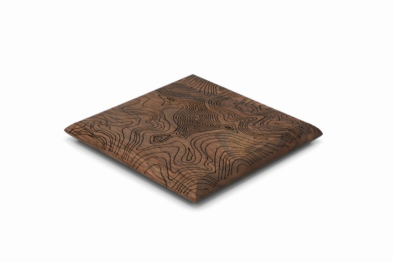 May include: A square wooden coaster with a brown wood grain finish and a black topographic map design.