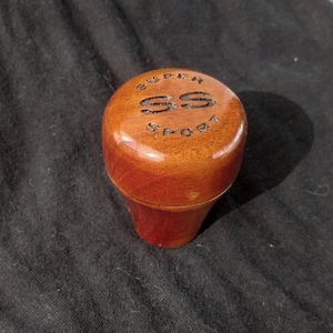 May include: A wooden gear shift knob with the words "SUPER SS SPORT" engraved on the top.