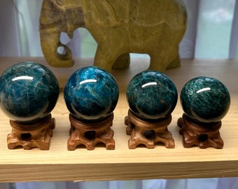 May include: Four blue apatite crystal spheres on wooden stands. The spheres are different sizes and have a smooth, polished finish.