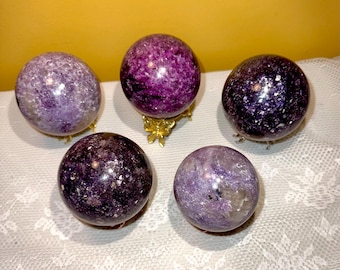 May include: Five purple and white lemurian quartz crystal spheres on gold stands. The spheres are polished and have a sparkly finish.