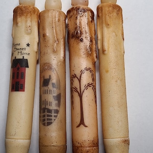 May include: Four decorative LED candles with a rustic, distressed finish. Each candle features a different design: a house with the text "Home Sweet Home", a building with a fence, a willow tree, and a plain candle.