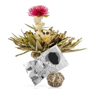 May include: A single blooming tea bud with a pink flower on top, surrounded by green leaves. The tea bud is packaged in a silver foil pouch.