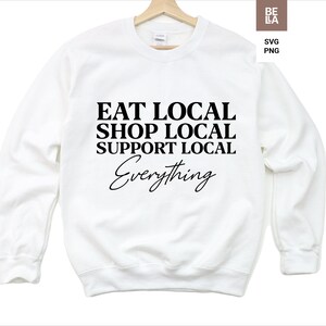 May include: White sweatshirt with black text that reads "Eat Local Shop Local Support Local Everything".
