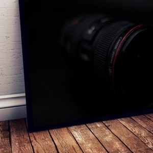 May include: A close-up of a black camera lens with a red ring around the edge. The lens is in focus, and the background is blurred.