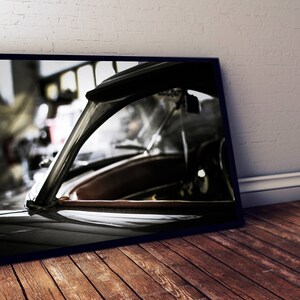 May include: A black and white photograph of a vintage car's rear window and roofline. The car is in a garage and the window is partially open. The photo is framed in a black frame.