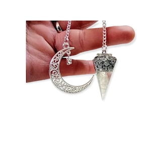 Può includere: Un pendolo color argento con un cristallo trasparente e appuntito e un ciondolo decorativo a forma di mezzaluna. Il pendolo ha una catena e una parte superiore in cristallo sfaccettato. Il ciondolo a forma di luna ha una stella.