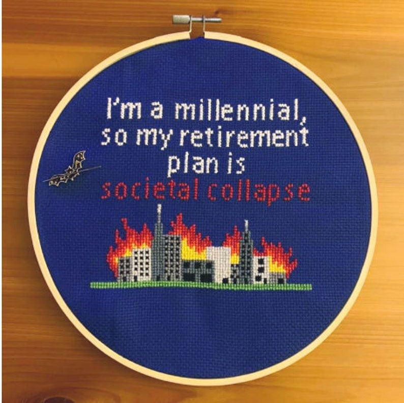 May include: A blue embroidery hoop with a white wooden frame. The embroidery depicts a cityscape on fire with the text "I'm a millennial, so my retirement plan is societal collapse".