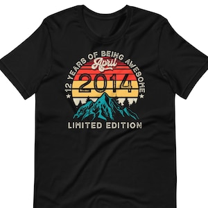 Peut inclure: T-shirt noir avec un motif rétro. Le motif présente le texte "12 YEARS OF BEING AWESOME" avec "April 2014" au centre, au-dessus d'un graphique de montagne. Les mots "LIMITED EDITION" sont en dessous.