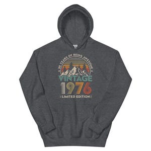 May include: A dark gray hooded sweatshirt with a graphic design. The design features the text "50 YEARS OF BEING AWESOME" above a mountain scene and the year "1976" in a vintage style. The words "Limited Edition" are below.