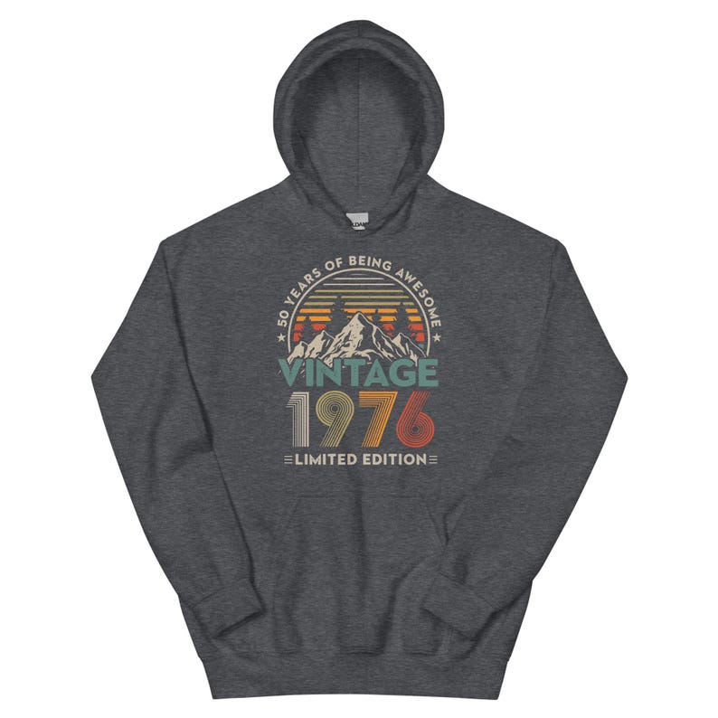 May include: A dark gray hooded sweatshirt with a graphic design. The design features the text "50 YEARS OF BEING AWESOME" above a mountain scene and the year "1976" in a vintage style. The words "Limited Edition" are below.