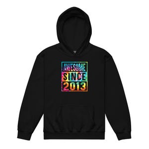 May include: Black hooded sweatshirt with a front pocket and drawstring. The front features a colourful tie-dye square with the words "AWESOME SINCE 2013" in white. The hoodie has a hood and long sleeves.